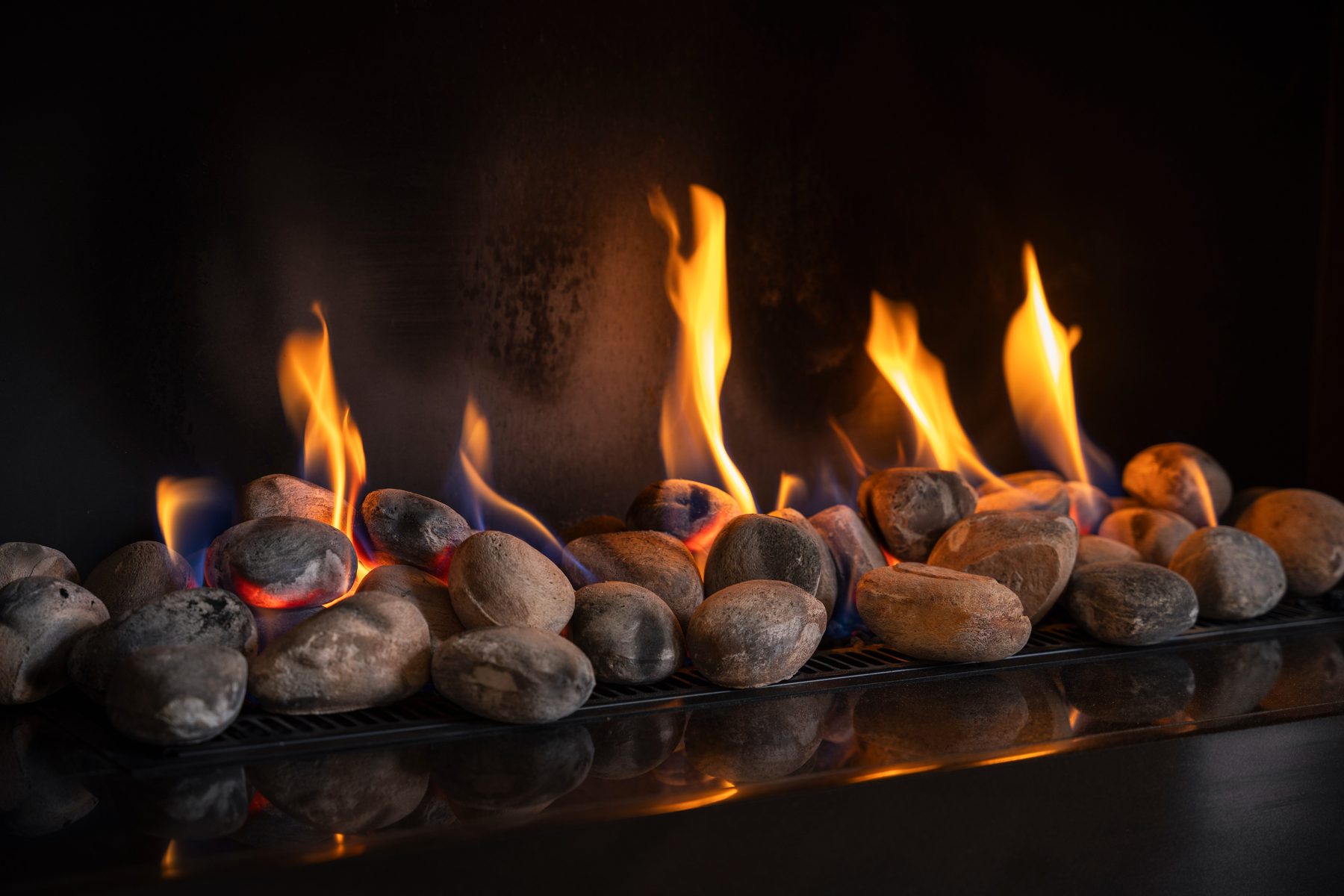 Living flame gas fireplace with natural pebble bed and reflective hearth — bespoke living room by Hafferty Interiors