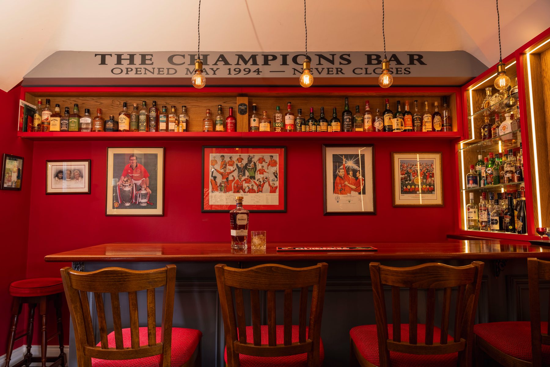 Bespoke full-room home bar with red joinery, oak spirits shelf and illuminated display cabinet — The Champions Bar by Hafferty Interiors
