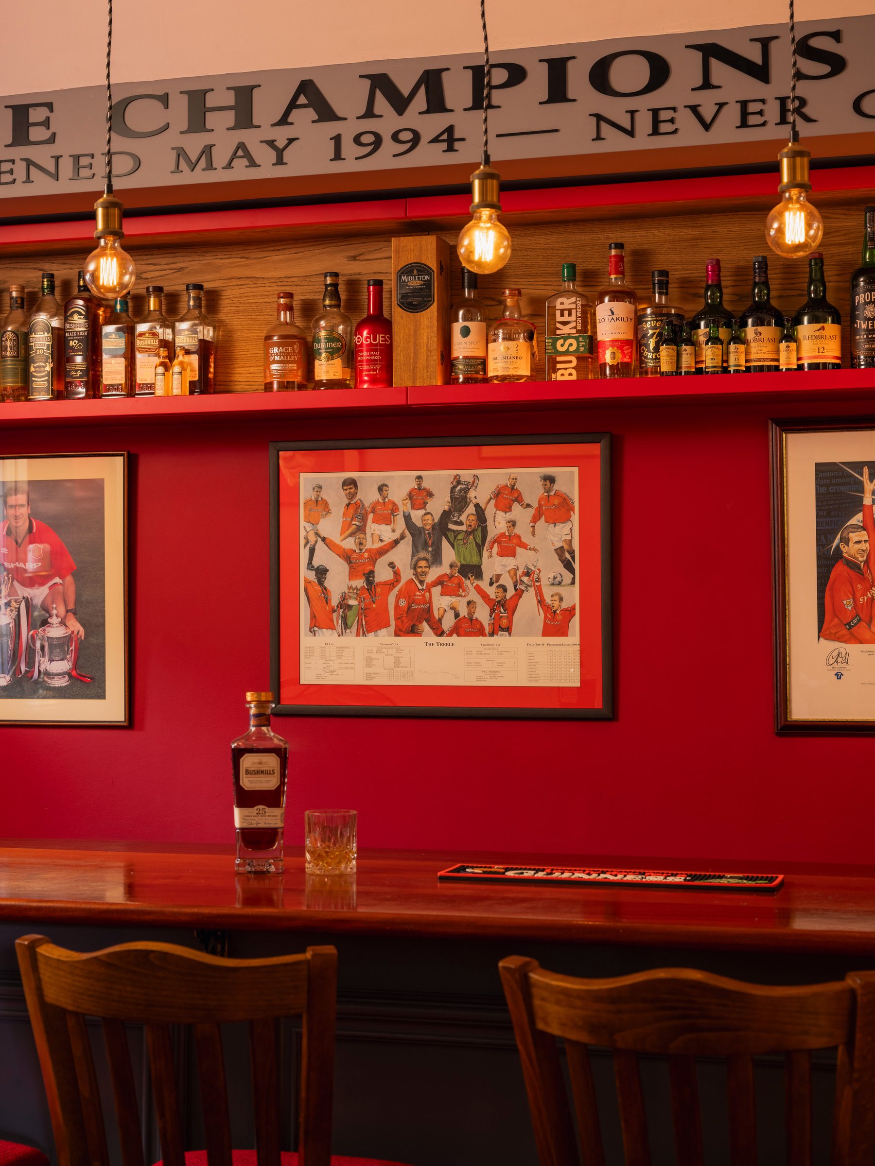 The Treble print displayed above the bar counter with whiskey shelf and Edison pendants — The Champions Bar by Hafferty Interiors