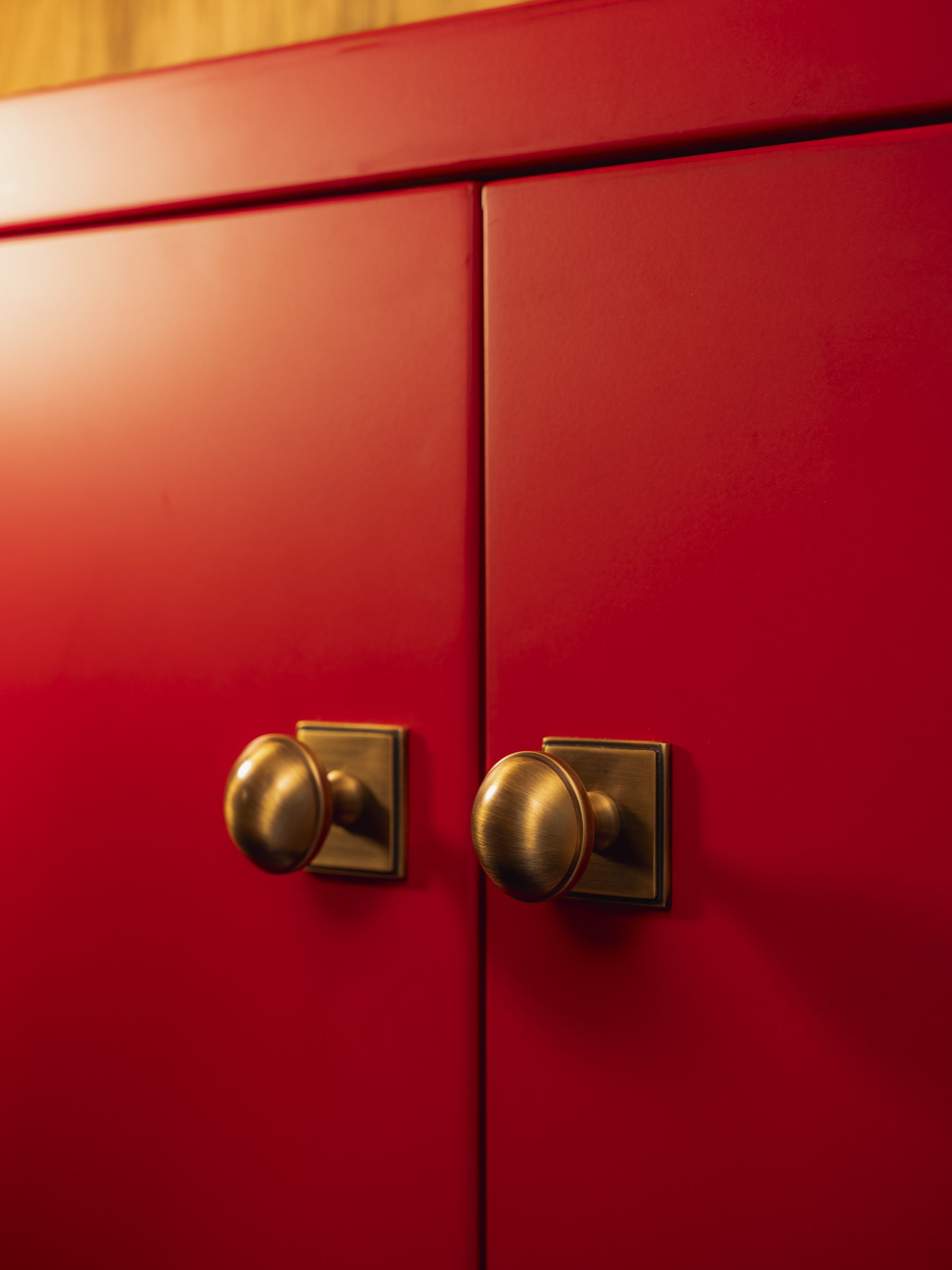 Antique brass oval door knobs on Manchester United red painted cabinetry — The Champions Bar detail by Hafferty Interiors