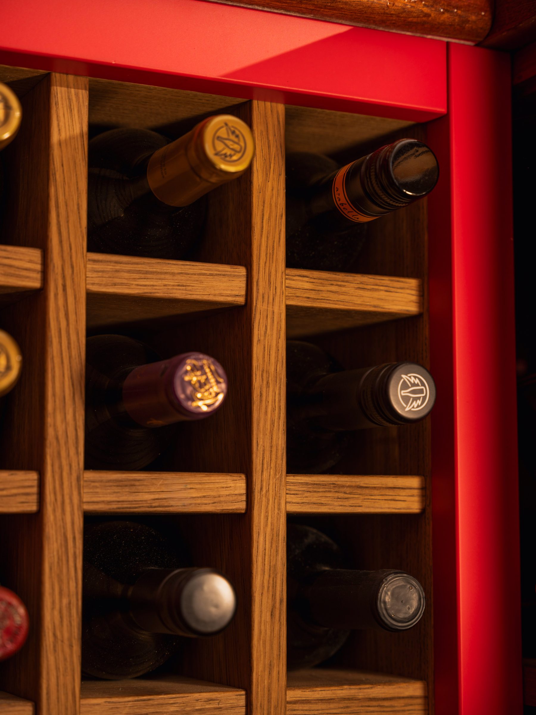 Integrated oak wine rack with individual bottle cells within red joinery — The Champions Bar by Hafferty Interiors