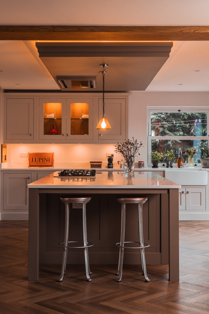 Bespoke in-frame kitchen with glass-fronted wall cabinets, warm oak backing and integrated gas hob in island — Hafferty Interiors