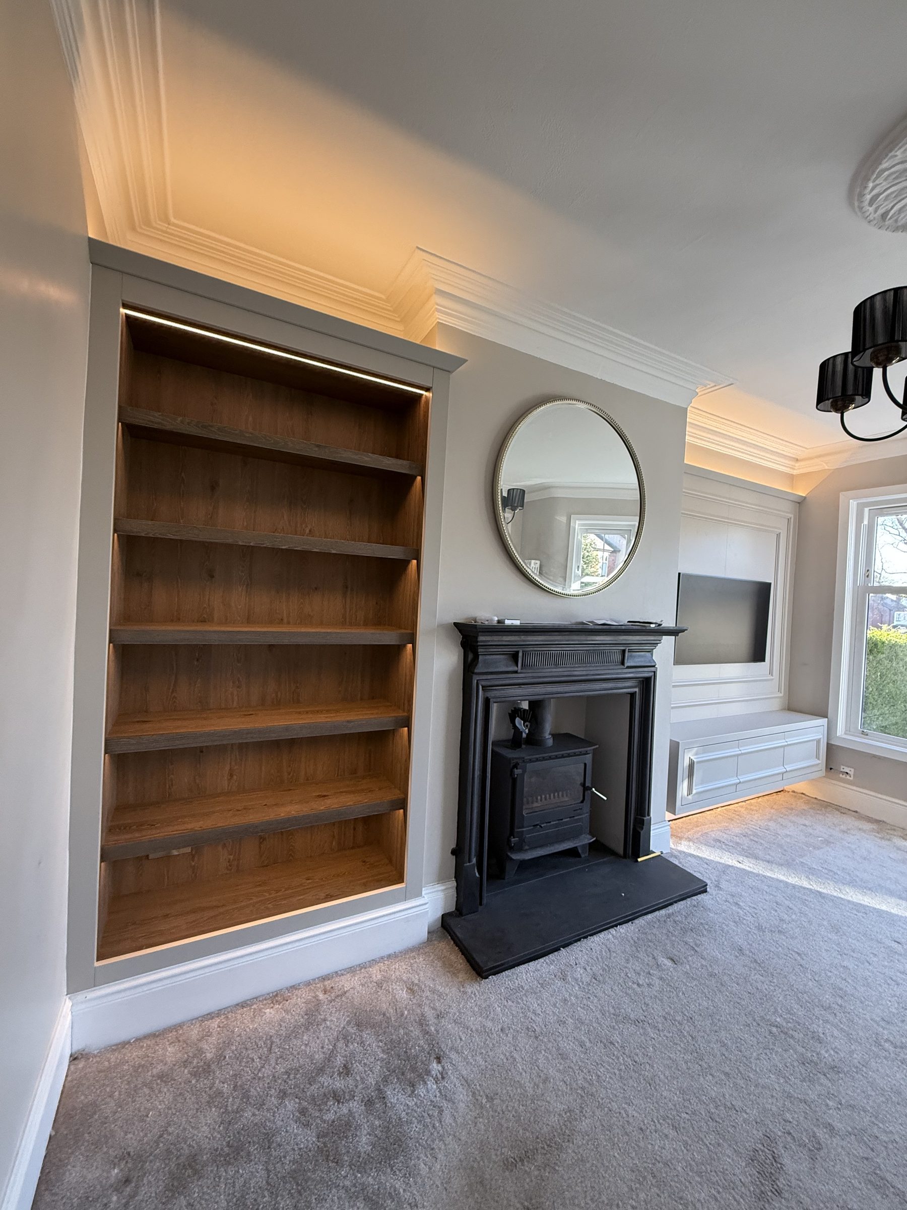 Bespoke oak alcove bookcase with LED lighting alongside period cast iron fireplace — Hafferty Interiors